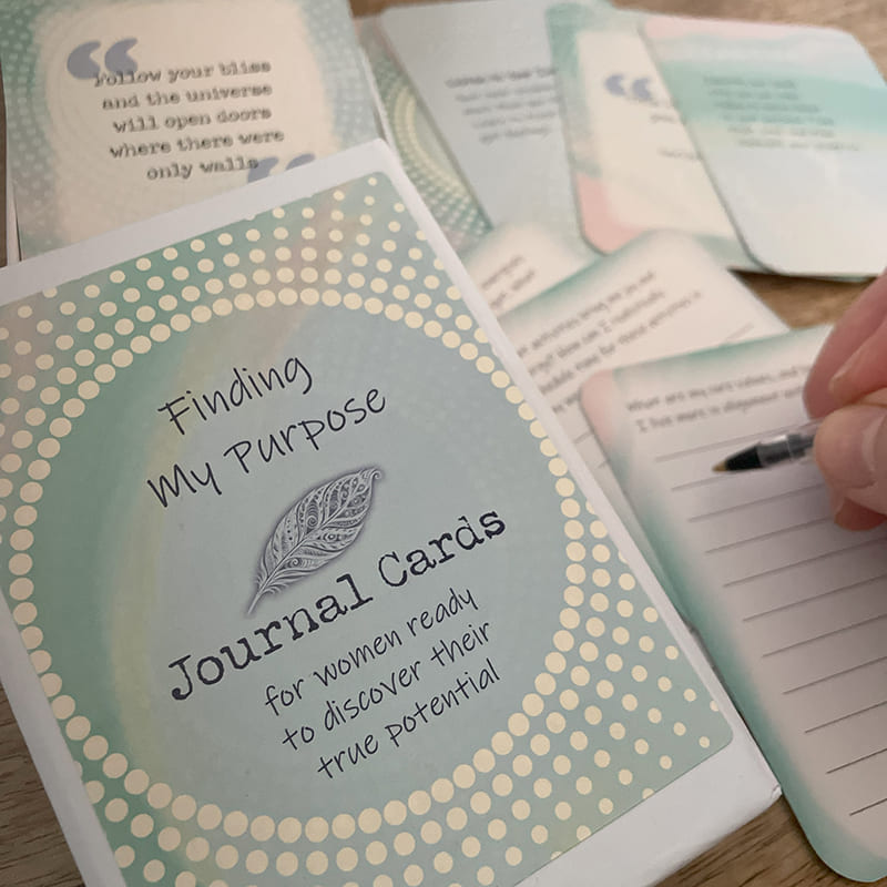 Finding My Purpose Journal Cards – purpose-finding deck box beside hand journaling on a lined prompt card, with motivational quote cards nearby.