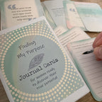 Finding My Purpose Journal Cards – purpose-finding deck box beside hand journaling on a lined prompt card, with motivational quote cards nearby.