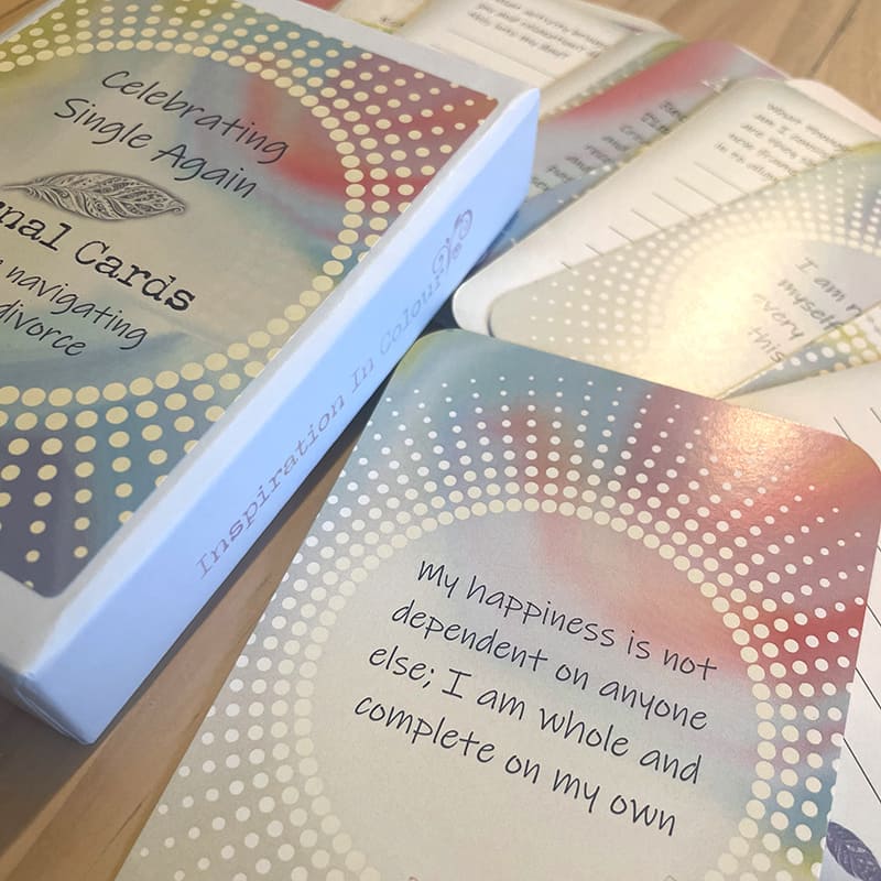 A close-up of the card box spine labeled "Inspiration In Colour," next to an affirmation card reading "My happiness is not dependent on anyone else; I am whole and complete on my own," with other cards fanned nearby.
